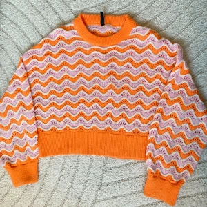 Missonicardigan - Superfin stickad tröja i orange och ljusrosa med vågigt mönster. Tröjan har ribbade muddar och är croppad i modellen. Perfekt för att sticka ut lite med färg och mönster! 💕
