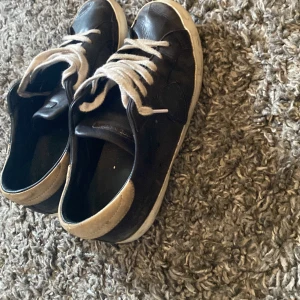 Svarta sneakers från Philippe Model - Svarta sneakers från Philippe Model i skinn med vita snören och vit sula. Hälpartiet är beige och skon har en klassisk låg profil. Perfekta för dig som gillar stilrena och tidlösa sneakers med premiumkänsla.