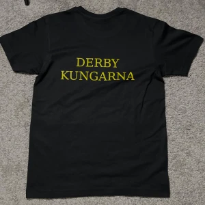 AIK T-shirt - Svart t-shirt med tryck i gult. Framsidan har siffran '1891' och baksidan texten 'DERBY KUNGARNA'. Halva summan går till tifogrupperna, alla storkar finns