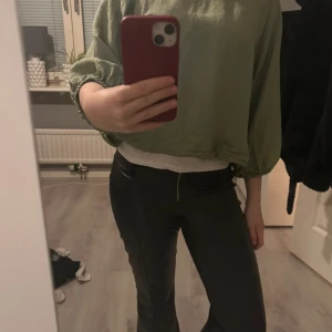 Ljusgrön croppad blus - Säljer en ljusgrön croppad blus med långa, lite puffiga ärmar och resår i nederkant och ärmslut. Blusen har en enkel rund halsringning och en liten öppning med knapp i nacken. Perfekt för en avslappnad och trendig look.