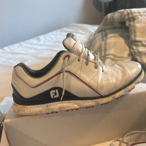 Vita golfskor från FootJoy - Säljer ett par vita golfskor från FootJoy med namn PRO sl. Vita till största del med blå och röda detaljer 