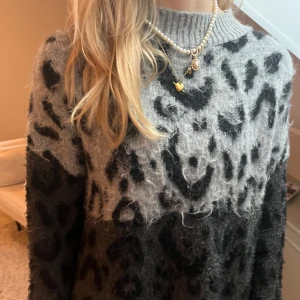 Grå och svart leopardmönstrad stickad tröja från Mango -  stickad tröja från Mango i grått och svart med leopardmönster. Tröjan har rund halsringning och långa ärmar.