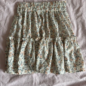 Blommig volangkjol - Supersöt kort kjol med blommigt mönster! Kjolen har volanger och bred resår i midjan för en bekväm passform. Perfekt för varma dagar och enkel att styla.