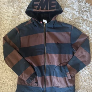 Randig hoodiejacka från Element Skate - Säljer en hoodiejacka från Element med breda svarta/gråa och bruna ränder. Jackan har dragkedja, huva med stor logga och mjukt svart foder på insidan. Praktiska fickor framtill och ribbade muddar vid ärmslut. Lite små skavanker och ett litet hål vid ena fickan. Vet ej storlek men den är nog Large, kan skicka mått om man vill ha! :) 