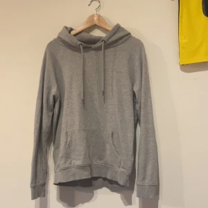 Grå hoodie  - En enkel och stilren grå hoodie med huva. Tröjan har en stor magficka och långa ärmar. Perfekt för en avslappnad look.