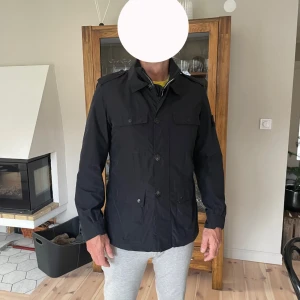 Svart jacka från Stone Island - Säljer en svart jacka från Stone Island med klassisk logotyp på vänster ärm. Jackan har krage, knäppning med knappar framtill och två bröstfickor med lock. Perfekt för dig som vill ha en stilren look. Kom med egna prisförslag. Nypris : 9000kr
