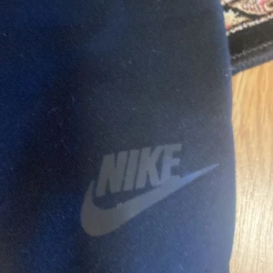 Svart jacka från Nike med dragkedja - Säljer en svart jacka från Nike med hel dragkedja framtill och en vertikal bröstficka med dragkedja. Jackan har en stilren design och Nike-logga på ärmen. Perfekt för dig som gillar sportig stil. Jag har tyvärr inte änvänt den eftersom den inte passade men därför vill ja iallafall få mina pengar tillbaka.