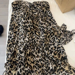 Axelbandslös leopardklänning - Säljer en snygg axelbandslös klänning med leopardmönster. Klänningen har volangdetaljer. Säljer då den är för stor för mig vid bysten.