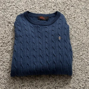 Blå kabelstickad tröja från Morris - Säljer en blå kabelstickad tröja från Morris med deras klassiska logga broderad på bröstet. Tröjan har rund halsringning och långa ärmar. Perfekt för dig som gillar stilrena och klassiska plagg. Tröjan är i storlek s men är lite urtvättad så skulle säga xs 