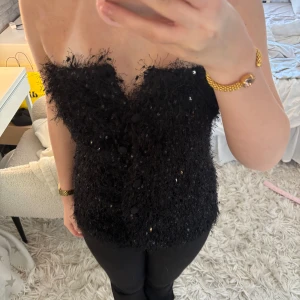 Svart glittrig tubtopp - Säljer en svart tubtopp med glittriga paljetter och fluffig textur. Toppen är axelbandslös och är perfekt för festligare tillfällen! Säljer då den var för stor för mig💖