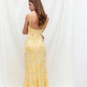 Gul långklänning med spetsdetaljer - Kollar intresset på denna Elegant gul långklänning med smala axelband och vackra spetsapplikationer. Klänningen har figurnära passform och öppen rygg, perfekt för speciella tillfällen. Materialet ger en lyxig känsla och de blommiga spetsdetaljerna gör den extra unik. Aldrig använd och är slutsåld