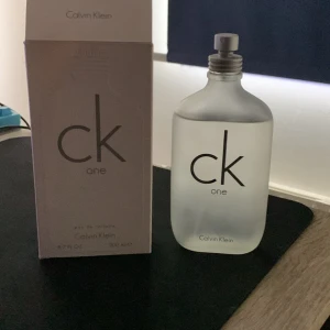 CK One Eau de Toilette 200 ml - Fräsch och ikonisk unisexparfym från Calvin Klein, CK One. Kommer i en frostad glasflaska med minimalistisk design och silverfärgad skruvkork. Volymen är 200 ml. Perfekt för dig som gillar rena och lätta dofter.