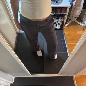 Grå kostymbyxor  - Snygga grå kostymbyxor med diskreta vita kritstrecksrand. Byxorna har normal passform och raka ben, samt låg/medel midja. Perfekta för en stilren och klassisk look.