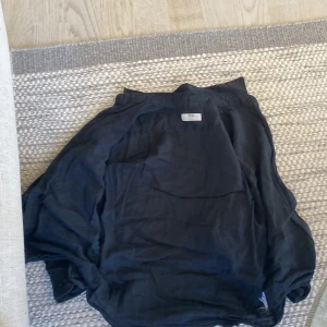 Svart linneskjorta från Uniqlo - Säljer en svart skjorta i linne från Uniqlo. Skjortan har klassisk krage, knäppning framtill och långa ärmar. Perfekt för dig som gillar en stilren och enkel look.