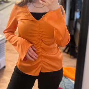 Orange omlottopp med v-ringning - Säljer en snygg orange omlottopp med v-ringning och långa utsvängda ärmar. Toppen har rynkade detaljer framtill som ger en cool look. Perfekt för dig som vill sticka ut med färg.