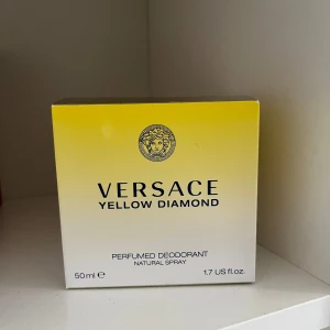 Versace Yellow Diamond parfumed deodorant  - Versace Yellow Diamond är en lyxig parfym i en elegant glasflaska med en stor, diamantformad gul kork. Doften är fräsch och feminin, och flaskan rymmer 50 ml. Förpackningen är gul och vit med Versaces klassiska logotyp.