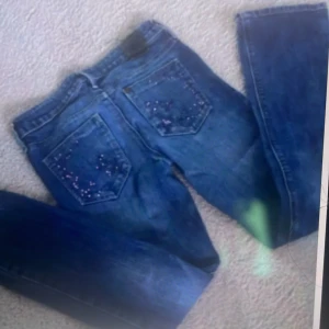 Blå jeansbyxor med broderade bakfickor från K Star - Säljer ett par klassiska blå jeansbyxor från K Star med broderade detaljer på bakfickorna. Byxorna har normal passform och raka ben, samt knapp och dragkedja framtill. Perfekta för dig som gillar en tidlös jeanslook. Säljer för är för småa💕 priset kan diskuteras!!!!