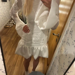 Vit kortklänning med volang och spetsdetaljer - Säljer en vit kortklänning med långärmade vida ärmar och vackra spetsdetaljer. Klänningen har en volang nertill och är figurnära upptill. Perfekt för dig som vill sticka ut med en romantisk och trendig look.