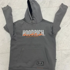 Grå hoodie och byxor från Hoodrich - Säljer ett grått set från Hoodrich med matchande hoodie och byxor. Hoodien har broderad logga framtill, huva med dragsko och magficka. Byxorna har tryckt logga längs benet och resår i midjan. Snygga orange detaljer på både tröja och byxor.