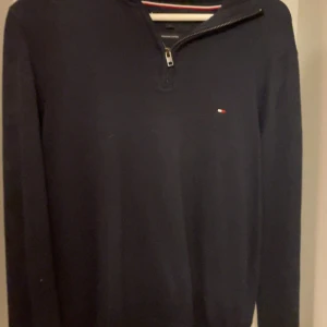 Mörkblå halvzip tröja från Tommy Hilfiger - Säljer en mörkblå långärmad tröja från Tommy Hilfiger med halv dragkedja och liten logga på bröstet. Tillverkad i bomull och har en klassisk, stilren look. Perfekt för lager-på-lager och passar till det mesta.
