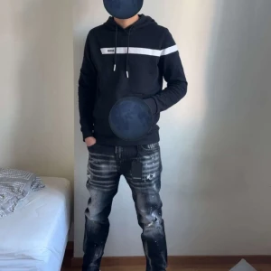 Dsquared2 - Säljer ett par svarta jeans från Dsquared2 med coola slitningar och vita färgstänk. Jeansen har en rak passform och klassisk femficksdesign. Perfekta för dig som vill ha en edgy och trendig stil.