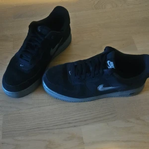 Svarta Nike Air Force 1 sneakers - Säljer ett par svarta Nike Air Force 1 sneakers med silverfärgad swoosh och svart ovandel. Klassisk modell med platt sula och rund tå. Perfekta för dig som gillar stilrena och tidlösa sneakers. Köptes före ca en månad sen på Nike.com.. Nästan nya, använd ett par gånger.