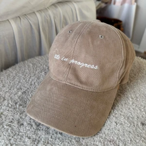 Beige keps från The Classics - Säljer en beige keps från The Classics med vit broderad text. Kepsen är i bomull och har klassisk form med böjd skärm och justerbar rem bak.