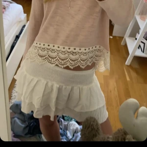 Vit volangkjol med spetsdetaljer - Säljer en superfin vit kjol med volanger och spetsdetaljer upptill. Kjolen har en kort längd och resår i midjan för en bekväm passform. Perfekt för dig som gillar romantisk och söt stil!