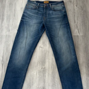 Blå jeans från Jack & Jones - Snygga blå jeans från Jack & Jones med klassisk femficksdesign och diskreta slitningar framtill. Jeansen har raka ben och normal passform, perfekt till vardags. Tidlös modell med bruna sömmar och knappgylf. Helt oanvända endast provade. Nypris är 900kr men säljer de för 700kr! Skriv för frågor! Storleken är 31/32
