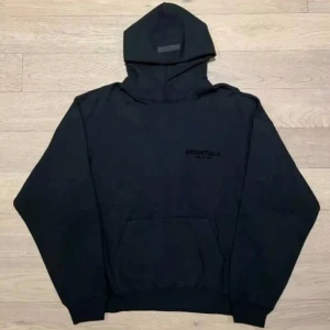 Svart hoodie från Fear of God Essentials - Säljer en svart hoodie från Fear of God Essentials. Klassisk modell med huva och magficka, diskret logga på bröstet. Perfekt för en stilren och avslappnad look.