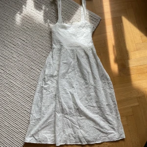 Vit klänning med knytaxelband - Säljer en söt vit klänning med broderade detaljer och knytbara axelband. Klänningen är ärmlös och har en lätt utställd kjol, perfekt för varma dagar. Från hm i storlek 36. 