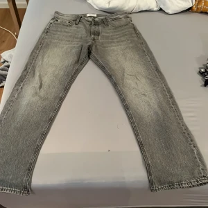Grå raka jeans från Jack and Jons - Säljer ett par grå jeans från Weekday med raka ben och klassisk femficksdesign. Jeansen har normal passform och är tillverkade i denim med en lätt tvättad look. Perfekta för en avslappnad stil.