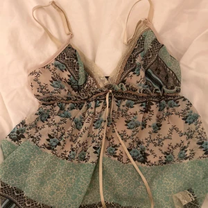 Somrig linnetopp med spets från Blasting - Säljer en söt linnetopp från Blasting med blommigt mönster i blått/grönt och beige, spetsdetaljer och tunna axelband. Toppen har knytband framtill och volang nertill. Inga defekter alls, använd fåtal gånger 💗Säljer för 89kr, priset kan diskuteras 💐 