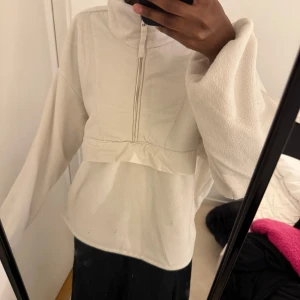 Vit fleece hoodie med halv dragkedja - Mysig vit hoodie i fleece med halv dragkedja framtill och hög krage. Tröjan har en oversized passform och långa ärmar, perfekt för kyliga dagar. Enkel och stilren design utan synliga loggor.