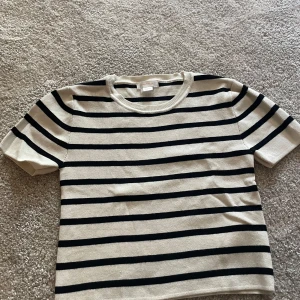 Randig kortärmad tröja från Gina Tricot - Säljer en beige och svart randig tröja från Gina Tricot. Tröjan har korta ärmar och rund halsringning. Perfekt för en avslappnad och stilren look.