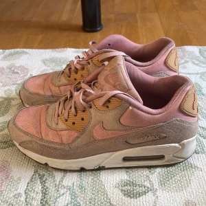 Nike Air Max 90 i rosa och beige - Säljer ett par Nike Air Max 90 i snygga rosa och beige toner med detaljer i ljusbrunt. Skorna har klassisk Air Max-sula, snörning och är tillverkade i en mix av skinn och syntetmaterial. Perfekta för dig som gillar streetwear och vill ha något unikt! lite små slitna men annars super fina och sköna skor!