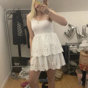 Vit somrig klänning med broderade detaljer - Söt vit klänning med två lager kjol och broderade blommönster. Kjolen har fina volangkanter och klänningen är perfekt för varma dagar. Använd en gång på skolavslutning förra året 