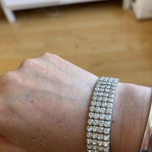 Glittrigt armband med strass - Säljer ett snyggt armband med flera rader glittrande strass i silverfärg. Perfekt för att ge outfiten extra bling! Armbandet är flexibelt och sitter bekvämt runt handleden.