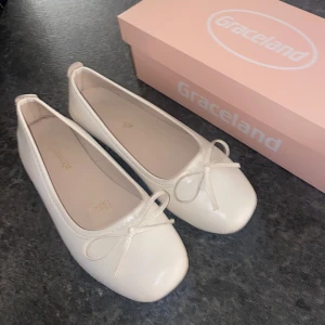 Vita ballerinaskor  - Säljer ett par stilrena rosa/beige/vita ballerinaskor i storlek 37 med söt rosettdetalj framtill. Skorna har platt sula, perfekta för en enkel och klassisk look. De är sparsamt använda men har fortfarande tecken på användning!