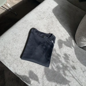 Svart träningst-shirt från Karhd - Svart teknisk t-shirt från Karhd med rund hals och korta ärmar. Tillverkad i ett lätt och ventilerande syntetmaterial, perfekt för träning. Diskret logga framtill nedtill. Snygg och funktionell för aktiva dagar.