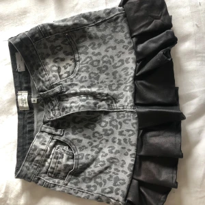 Grå jeanskjol med leopardmönster och volang - Cool grå jeanskjol från H&M med leopardmönster och bred svart volang nertill. Kjolen har klassiska jeansfickor fram och bak samt bälteshällor. Perfekt för dig som vill sticka ut lite extra.