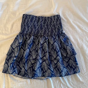 Mini kjol - Supersöt blå kjol med vitt grafiskt mönster och bred smock i midjan. Kjolen är kort och har ett tunt, lätt material med ett extra lager underkjol. Det finns inbyggda short och midjebandet kan man göra lågmidjat, mid waist och högmidjade. Skriva via funderingar och mera bilder hur kjolen sitter på💕