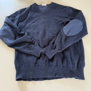 Mörkblå tröja med v-ringning från john henric  - Säljer en mörkblå tröja från john henric med v-ringning och matchande armbågslappar. Tröjan har långa ärmar och ribbade muddar vid ärmslut och nederkant. Perfekt för kyligare dagar och enkel att styla.