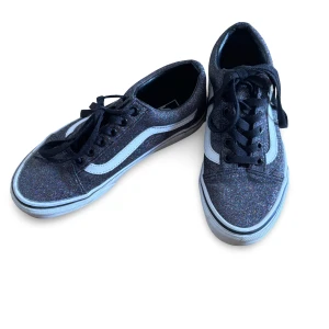 Svarta glittriga sneakers från Vans - Säljer ett par svarta Vans sneakers med glittereffekt och klassisk vit sula. Skorna har svarta snören och den ikoniska vita sidoremsan. Perfekta för dig som vill sticka ut med lite extra glans i vardagen.