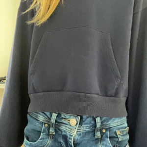 Mörkblå oversized hoodie - Mörkblå hoodie med stor magficka och huva. Tröjan har långa ärmar och bred mudd vid midjan. Perfekt för en avslappnad stil och passar bra till jeans.