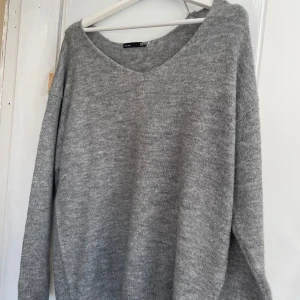 Grå stickad tröja med v-ringning - Mysig grå stickad tröja från H&M med v-ringad hals och långa ärmar. Perfekt för lager-på-lager och passar till både jeans och kjol. Enkel och stilren design som funkar året runt.