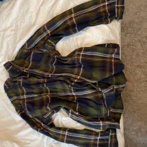Rutig skjorta från Dressmann - Säljer en rutig skjorta från Dressmann i grönt, blått och inslag av vitt och brunt. Skjortan har långa ärmar och klassisk krage. Perfekt för dig som gillar en avslappnad stil med lite färg.