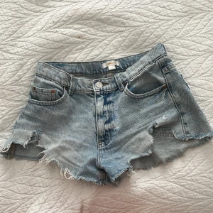 Ljusblå jeansshorts från Gina Tricot - Säljer ett par ljusblå jeansshorts från Gina Tricot med fransiga kanter och klassisk femficksdesign. Shortsen har låg midja och slitna detaljer för en cool look. Perfekta för varma dagar! Priset går att diskutera