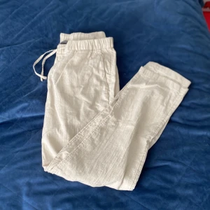 Beiga linnebyxor - Snygga och luftiga beiga linnebyxor med elastisk midja och dragsko. Perfekta för varma dagar och ger en avslappnad stil. Byxorna har raka ben och är tillverkade i ett lätt och svalt material.