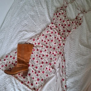 Blommig långklänning med slits och knytband - Superfin midiklänning med blommigt mönster. Klänningen har smala axelband med knyt samt slits på sidan. Perfekt för sommarens alla tillfällen!